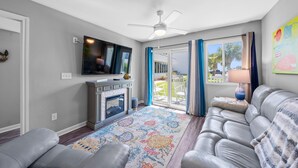 Una sala de estar con chimenea, ventilador de techo, televisor y vista al exterior a través de una puerta corrediza de vidrio.
