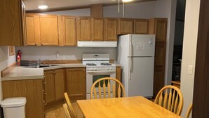 Una cocina funcional con armarios de madera, estufa blanca, refrigerador y mesa con sillas.