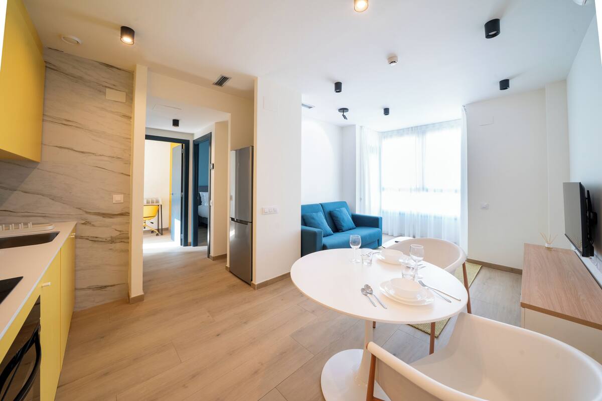Una cocina moderna con salpicadero de mármol, un comedor con mesa redonda y un sofá azul en un espacio habitable luminoso.
