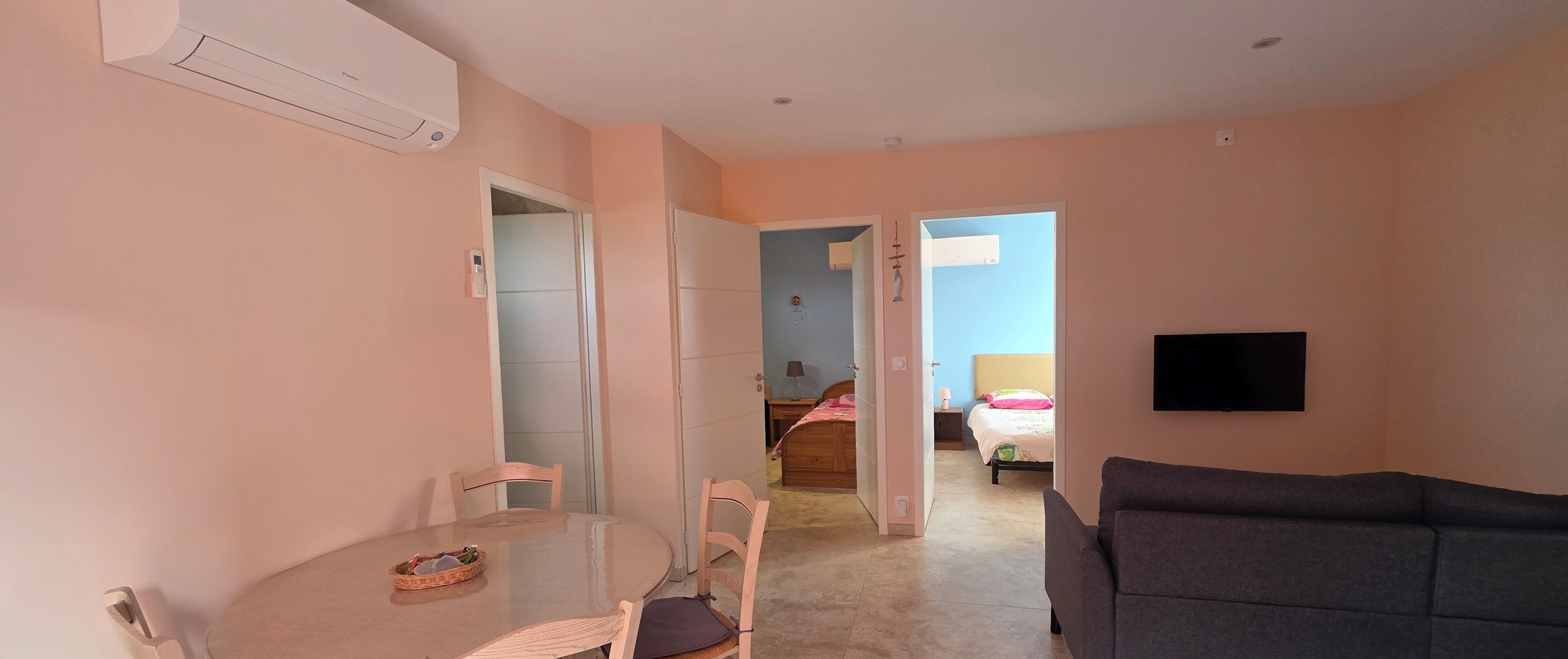 Un espace de vie compact comprenant une table à manger, un canapé et un téléviseur fixé au mur.