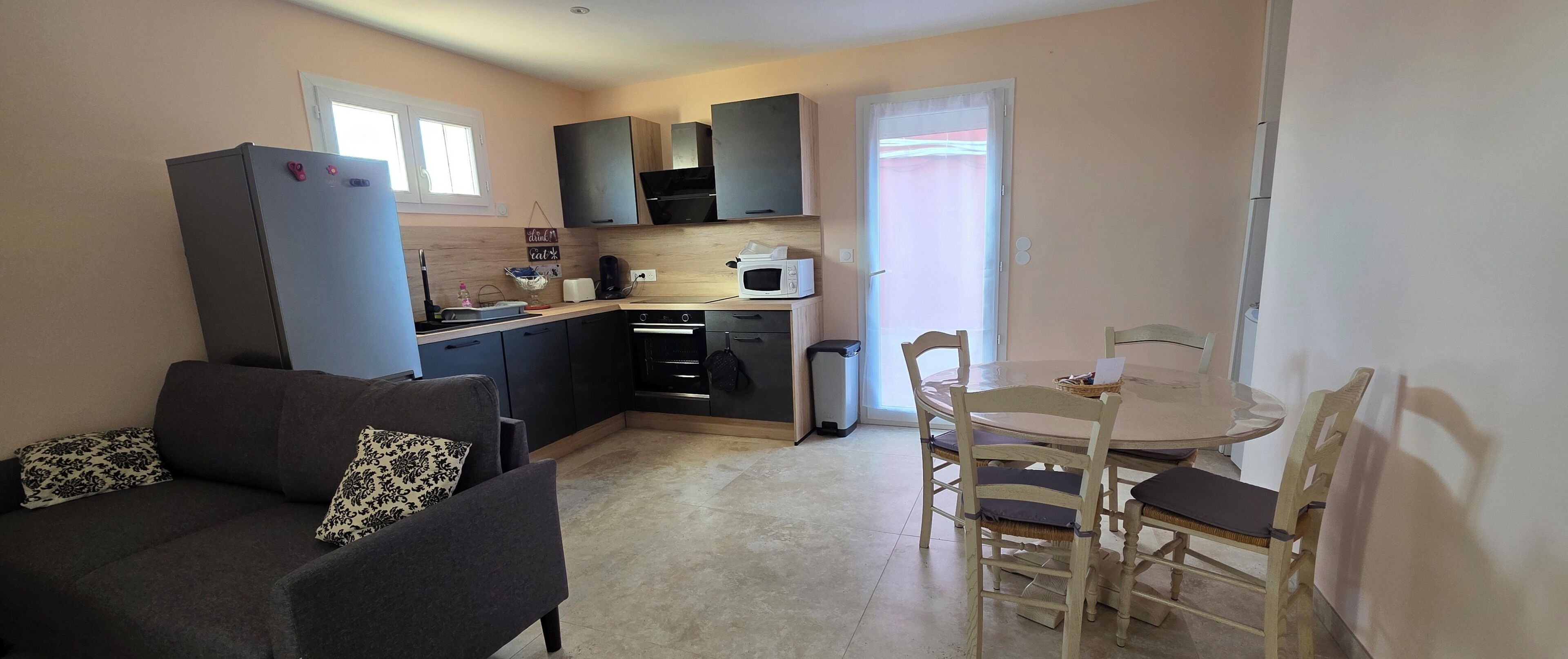 Een compacte woonruimte met een kitchenette, een eethoek met een ronde tafel en stoelen, en een bank met decoratieve kussens.