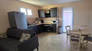 Ett kompakt bostadsutrymme med ett litet kök, en matplats med ett runt bord och stolar samt en soffa med mönstrade kuddar.