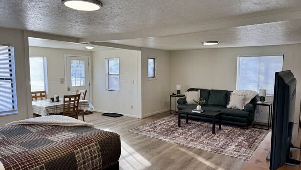 A spacious living room with a large bed, a sofa, a coffee table, and a TV. There is a dining area with a table and chairs. - Studio House - Central Location (Miles City)
