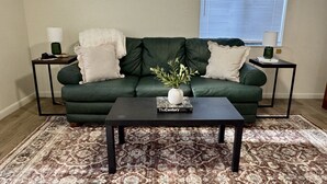 A living room with a green sofa, two side tables, a coffee table, and a patterned rug. - Studio House - Central Location (Miles City)