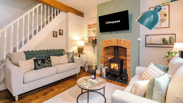 A cozy living room with a fireplace, a sofa, a coffee table, and a TV mounted on the wall. - Beautiful Cozy Cottage Home in Sandbach, Sleeps 4! (Cheshire East)