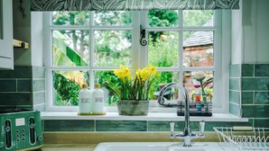 A kitchen with a window, a sink, a toaster, and a potted plant with yellow flowers. - Beautiful Cozy Cottage Home in Sandbach, Sleeps 4! (Cheshire East)