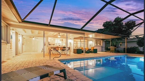 A swimming pool with a glass enclosure, a patio area with seating, and a view of the sky. - European Artistic Retreat (Cape Coral)