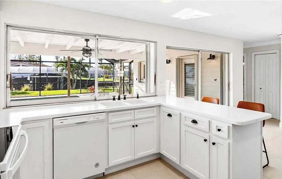 A modern kitchen with white cabinetry, a large window, and a view of a garden.