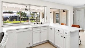 A modern kitchen with white cabinetry, a large window, and a view of a garden. - European Artistic Retreat (Cape Coral)