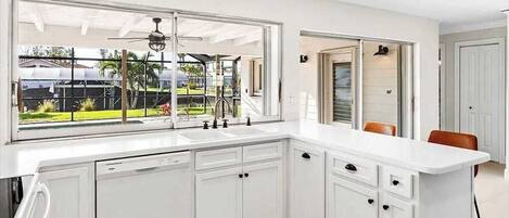 A modern kitchen with white cabinetry, a large window, and a view of a garden.