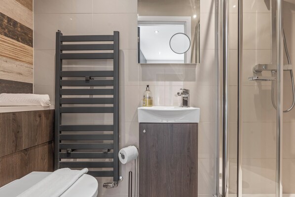A modern bathroom with a wooden towel rack, a sink with a mirror above it, and a glass shower enclosure.