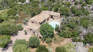 A stone building with a tiled roof surrounded by dense greenery and rocky terrain.