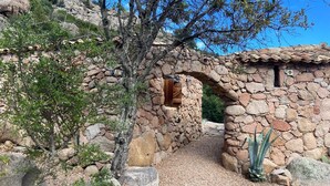 A stone building with a rustic, arched doorway and a small window, surrounded by natural vegetation and rocks.
