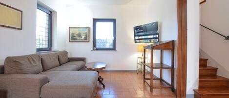 A living room with a sofa, a TV on a stand, a painting, and a staircase.
