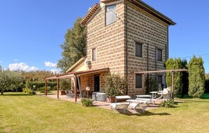 Une maison en pierre à deux étages, dotée d’un patio aménagé avec des meubles d’extérieur et un barbecue.