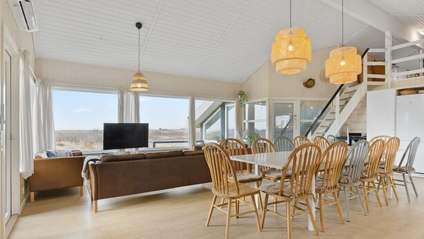 A spacious living area with a large window, a sofa, a dining table with chairs, and a staircase. - Cozy home in Løgstør with sauna (Løgstør)