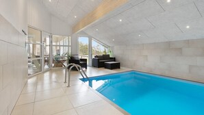 An indoor swimming pool with a glass wall, a wooden ceiling, and a seating area with a view of the outdoors. - Cozy home in Løgstør with sauna (Løgstør)
