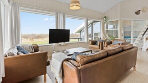 A spacious living room with a large window, a flat-screen TV, leather sofas, and a staircase leading to an upper level. - Cozy home in Løgstør with sauna (Løgstør)