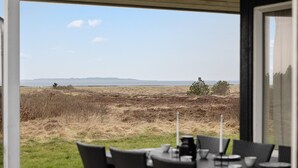 A dining area with a view of a grassy field and distant hills. - Cozy home in Løgstør with sauna (Løgstør)