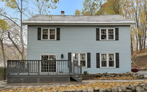 A two-story house with a front deck and stone wall.