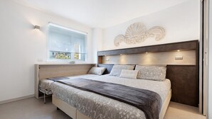 A modern bedroom with a large bed, built-in bedside tables, a window with a view, and a decorative wall piece. - Eco del Garda - Room 102 - Ground Floor, Mountain View (Tenno)