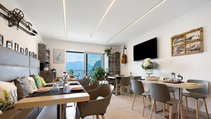 A modern dining area with a large window, a flat-screen TV, and a guitar on the wall. - Eco del Garda - Room 102 - Ground Floor, Mountain View (Tenno)