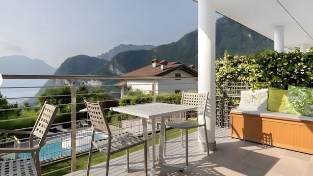A balcony with a pool, chairs, and a table, overlooking a mountainous landscape and a body of water. - Eco del Garda - Room 102 - Ground Floor, Mountain View (Tenno)