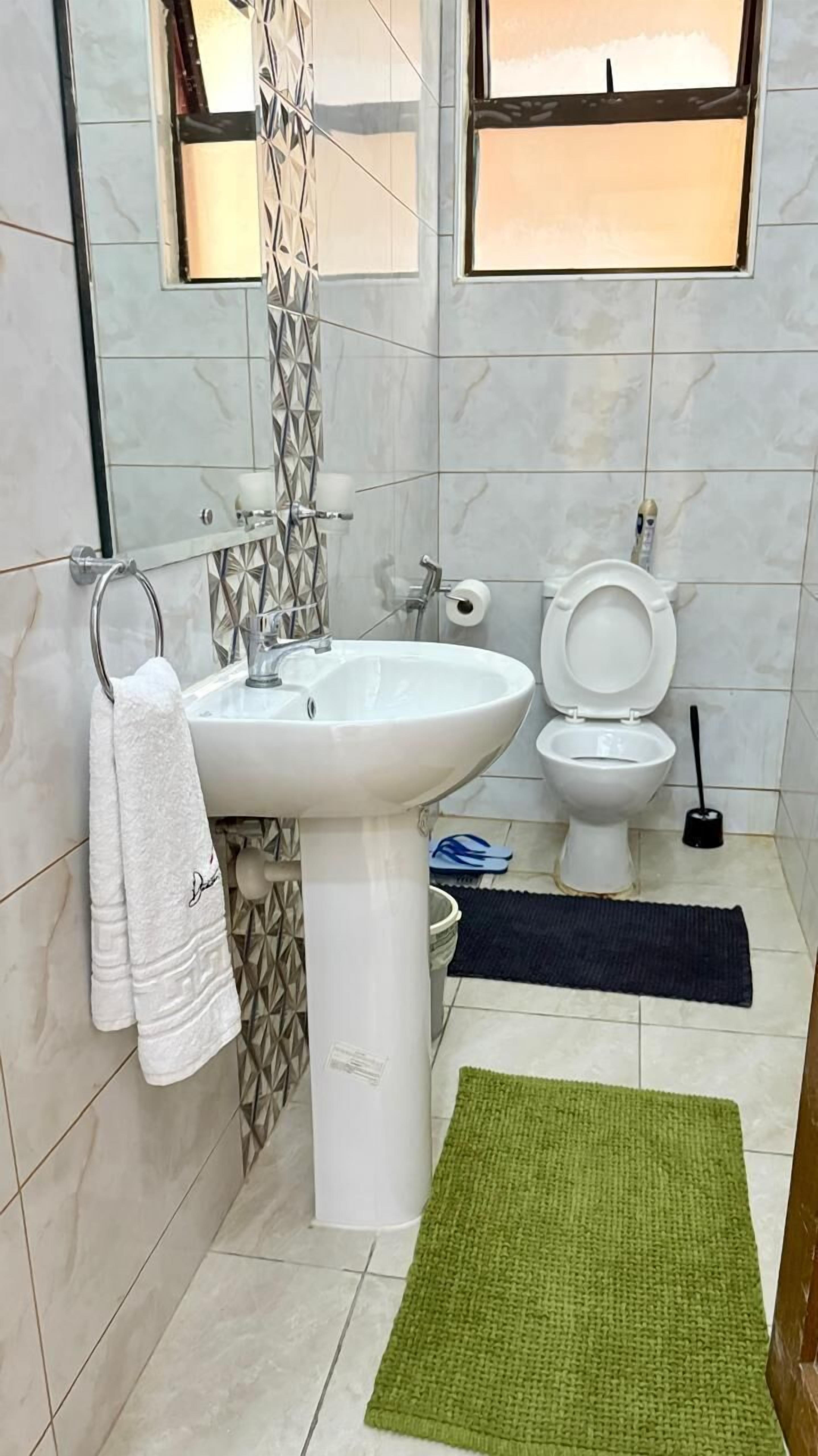 Un baño con lavamanos blanco, inodoro y una alfombra verde en el suelo.