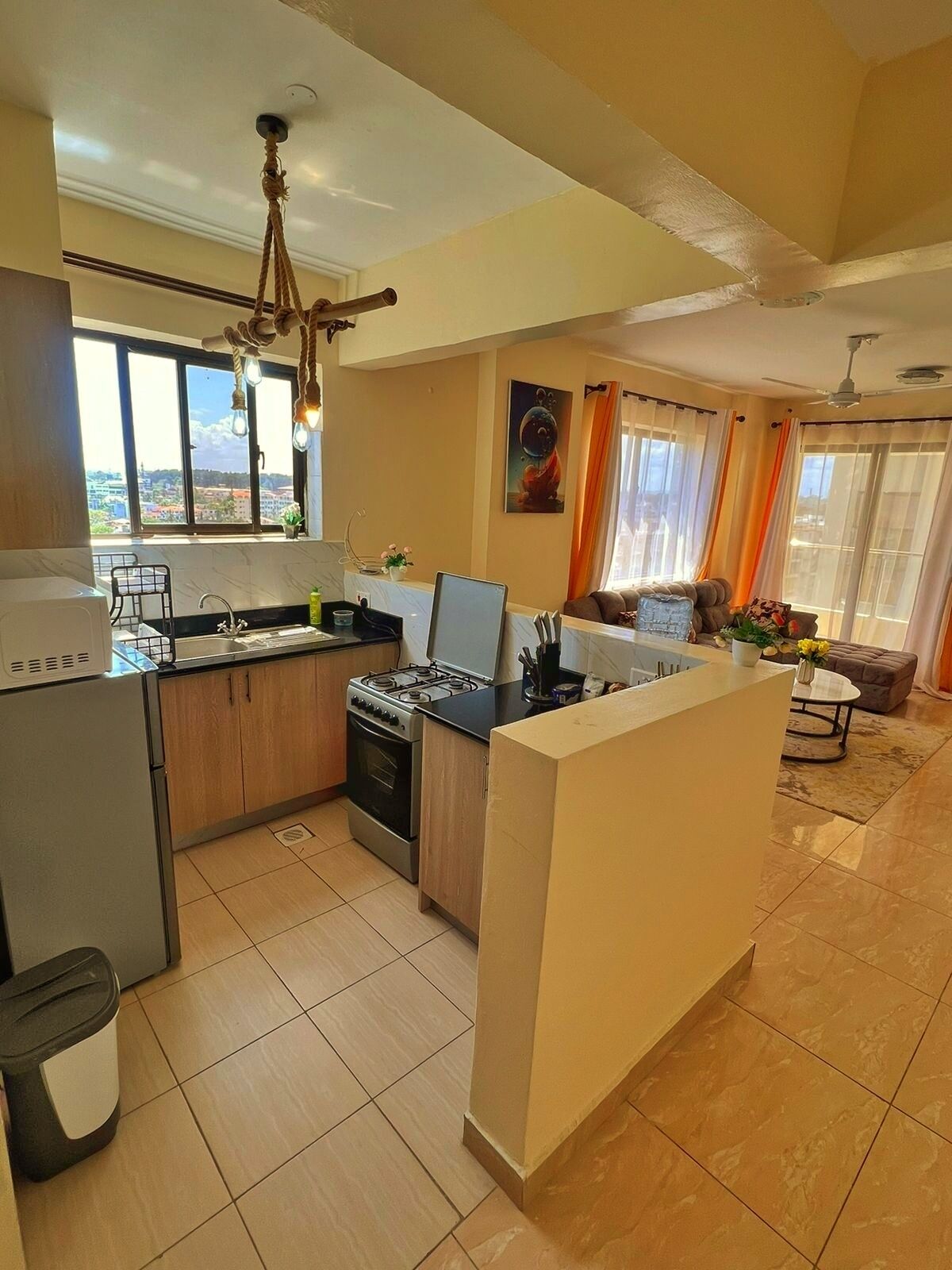 Una cucina moderna con isola centrale, una zona pranzo con divano e tavolo, e vista sulla città attraverso ampie finestre.