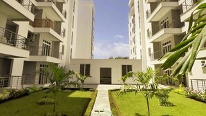 Un moderno edificio de apartamentos con varios balcones, un patio central con un sendero y pequeños árboles.
