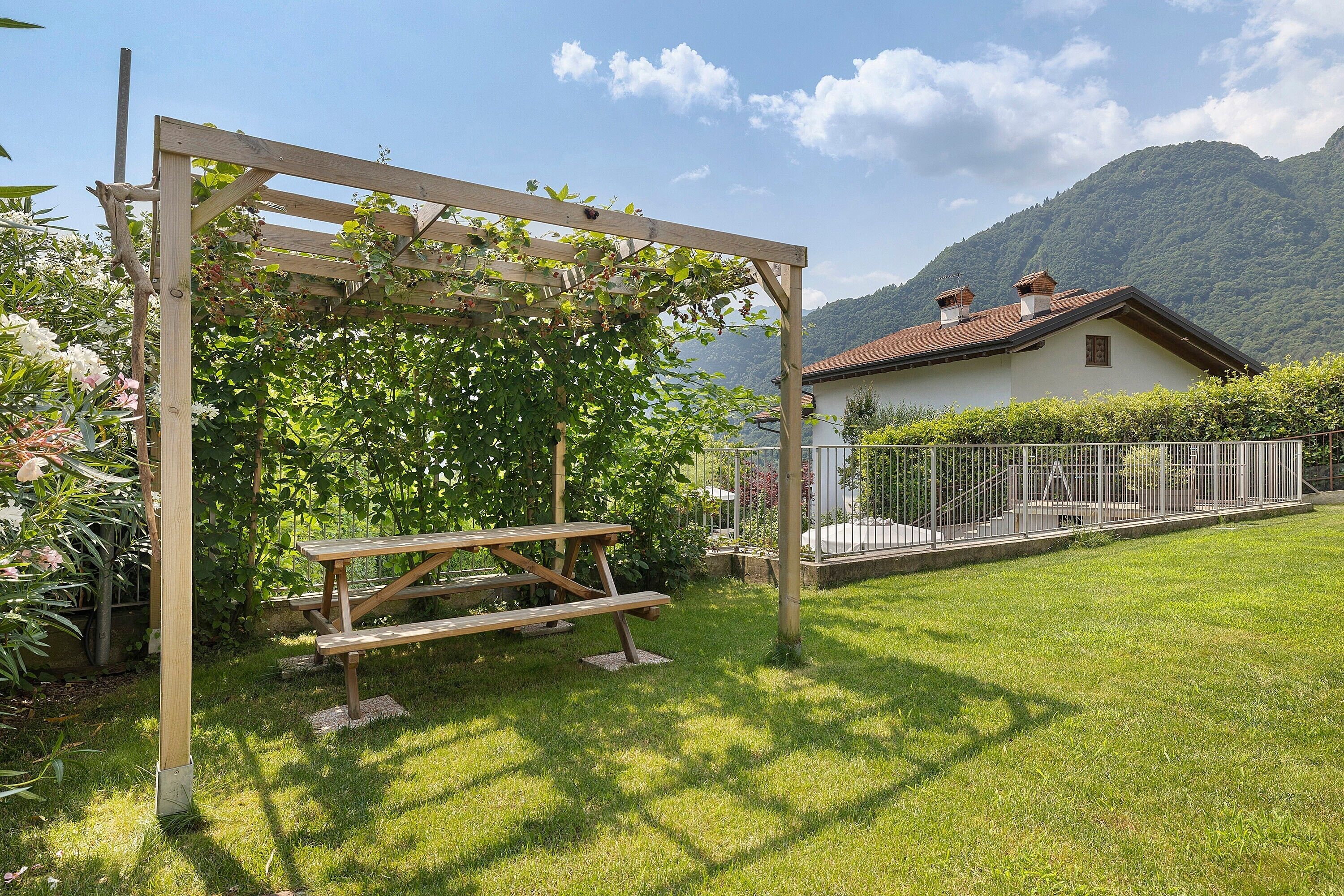 Eine Holzhütte mit einem Picknicktisch in einem grasbewachsen Garten mit Blick auf Berge.