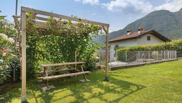 Eine Holzhütte mit einem Picknicktisch in einem grasbewachsen Garten mit Blick auf Berge.