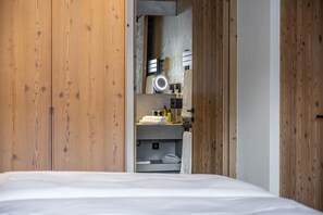 A bedroom with a wooden wardrobe, a bed, and a built-in mirror with a vanity.