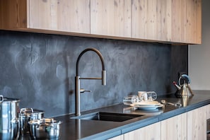 Une cuisine moderne avec un plan de travail foncé, des meubles en bois, des ustensiles de cuisine en acier inoxydable et une bouilloire posée sur le comptoir.