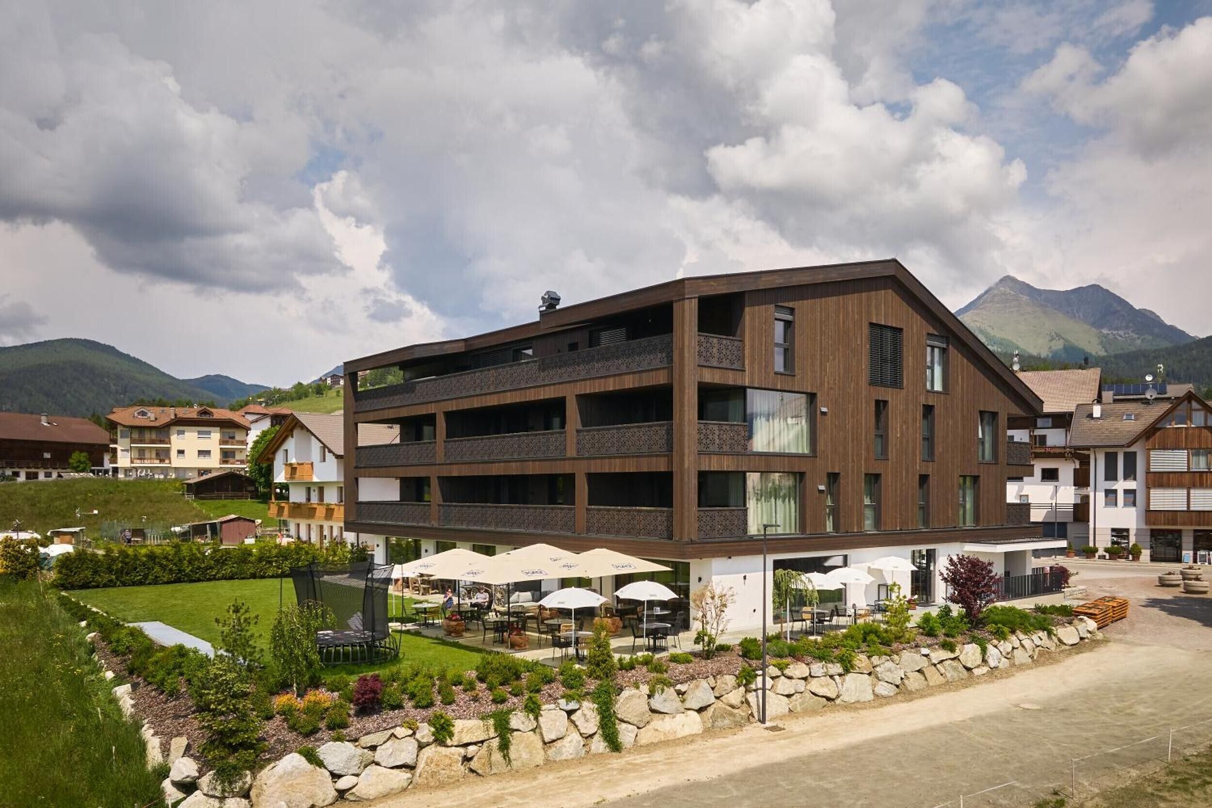 Um hotel moderno com vários andares, área de estar ao ar livre, um muro de pedra e montanhas ao fundo.
