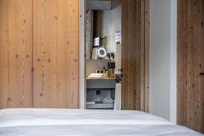 Une chambre avec une armoire en bois, un lit et un miroir intégré agrémenté d’une coiffeuse.