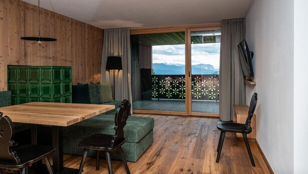 Ein Zimmer mit Holzboden, einem grünen Sofa, einem Holztisch und einem an der Wand befestigten Fernseher.