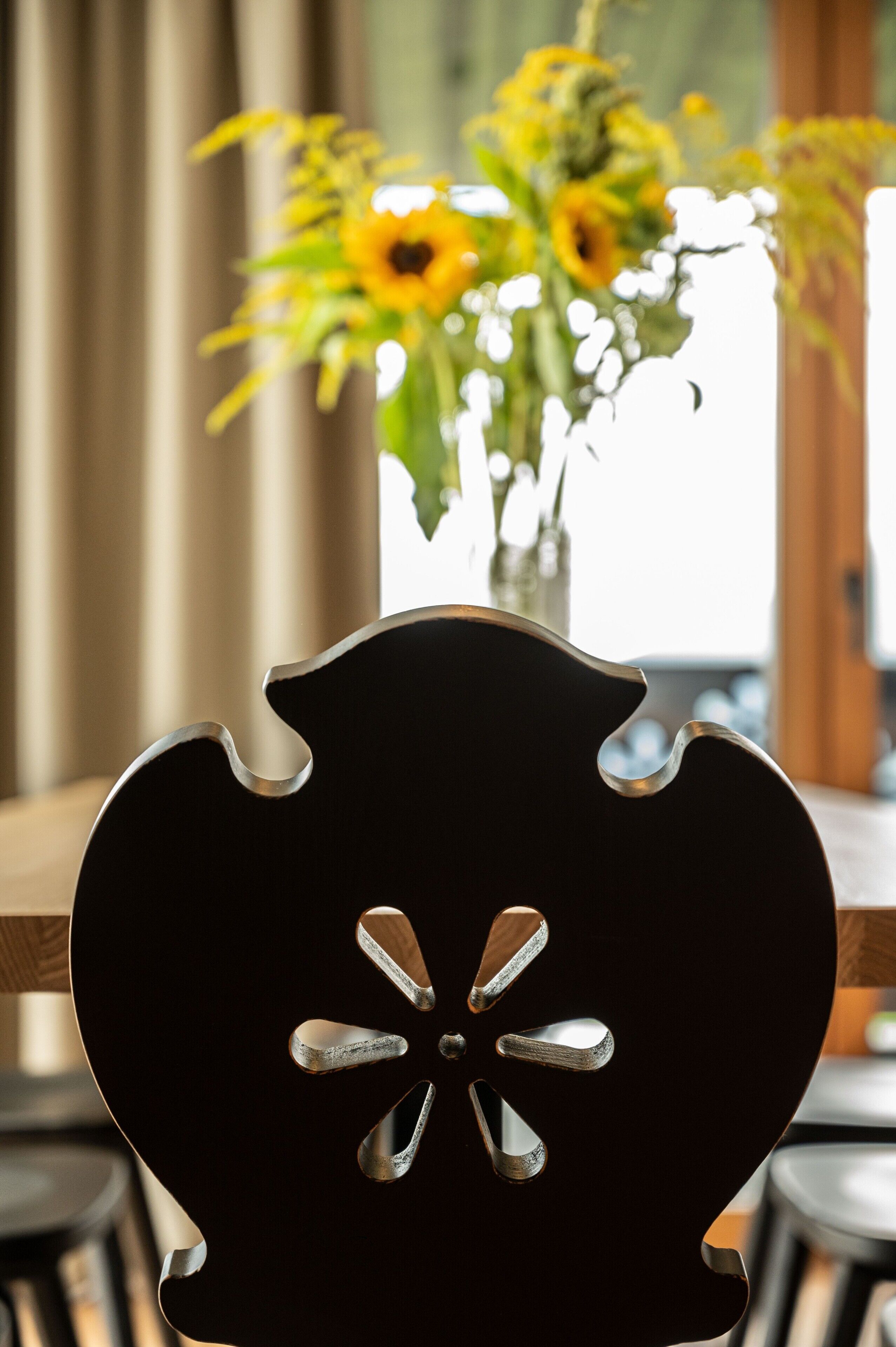 A chair with a unique back design and a vase of sunflowers in the background.