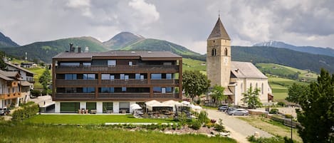 A modern building with a large windowed front, a church with a bell tower, and a mountainous backdrop.