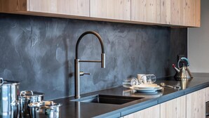 A modern kitchen with a dark backsplash, wooden cabinets, stainless steel cookware, and a kettle on the counter.