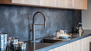 A modern kitchen with a stainless steel sink, wooden cabinets, and a marble backsplash.