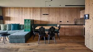 A modern kitchen with a wooden wall, a dining area with a green sofa and black chairs, and a built-in cabinet.