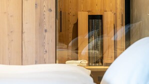 A wooden room with a bed, a small table, and a wall-mounted heater.