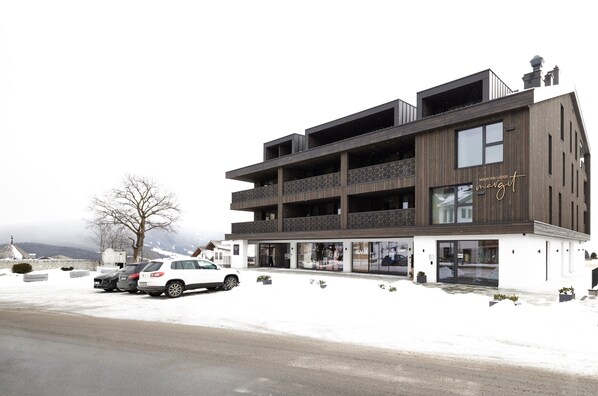 Un edificio moderno con varios balcones, un automóvil estacionado al frente y nieve en el suelo.