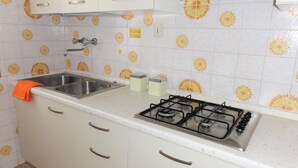 A kitchen with white cabinets, a stainless steel sink, a gas stove, and a tiled backsplash with a sunflower pattern. - Apartment in a Villa With Garden (San Michele al Tagliamento)