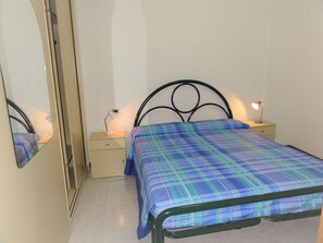 Un dormitorio con cama, mesita de noche, espejo y lámpara de pared.