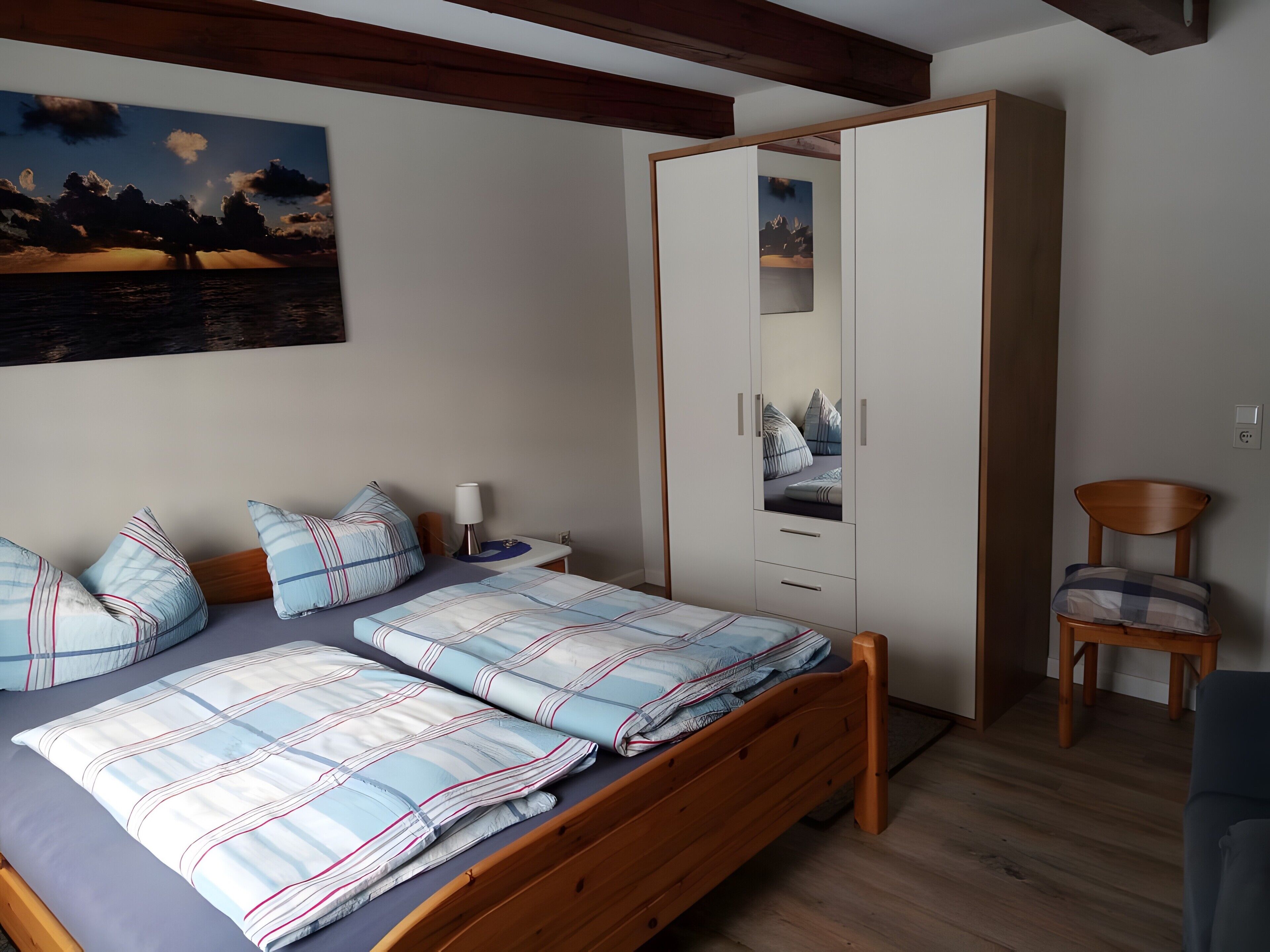 A bedroom with a bed, a wardrobe, a chair, and a painting on the wall.