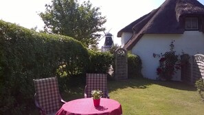 A garden with a round table and chairs, a windmill in the background, and a white building with a thatched roof. - Apartment 'Fewo Springflot' with Shared Terrace, Shared Garden and Wi-Fi (Pellworm)