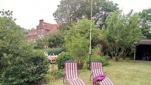 A garden with two striped lounge chairs, a table with chairs, and a building in the background.