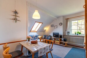 Kodikas huone, jossa on ruokapöytä, tuoleja, sohva, televisio ja ikkuna, jossa on verhot.